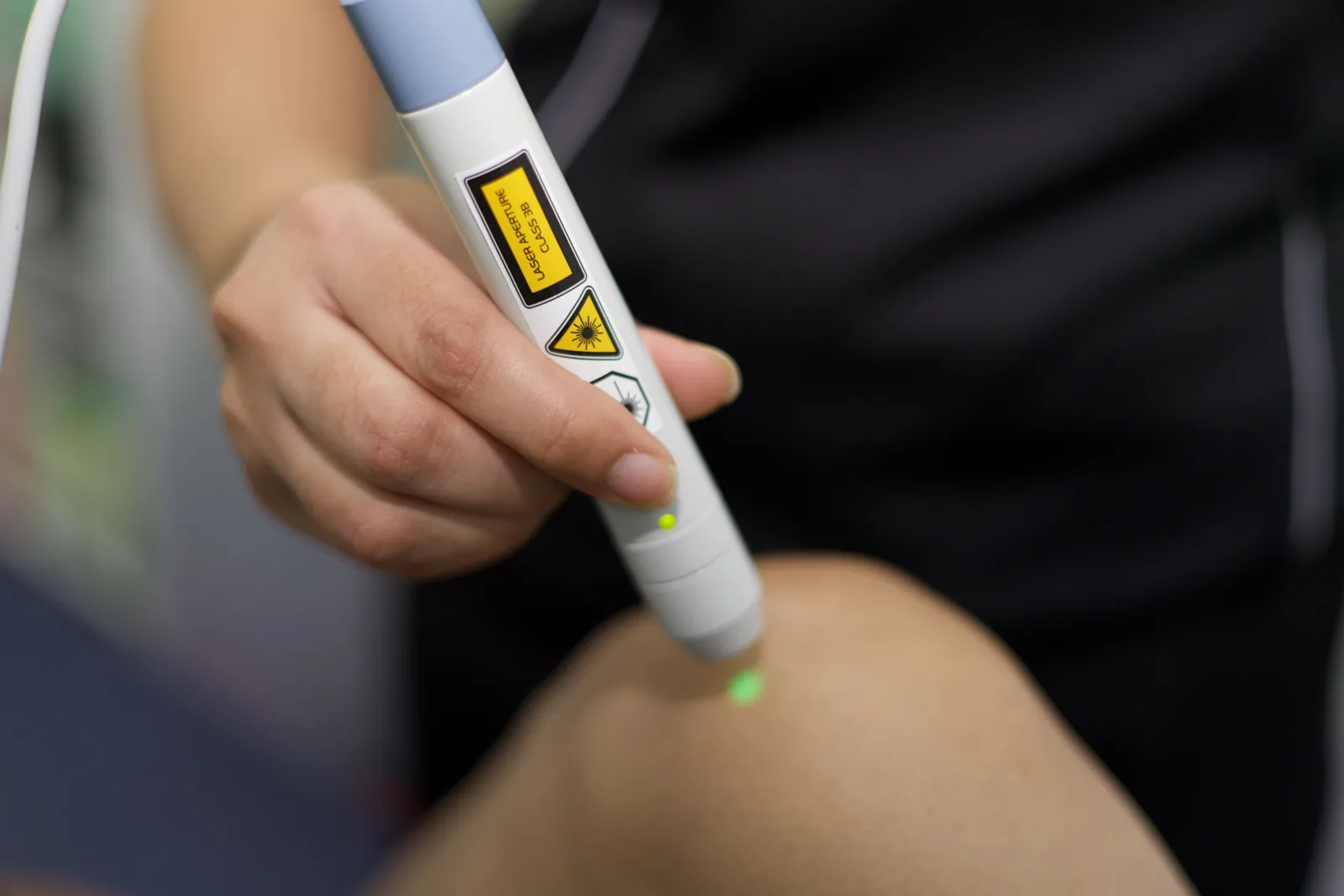A physiotherapist applying a therapeutic laser probe to a patient's knee