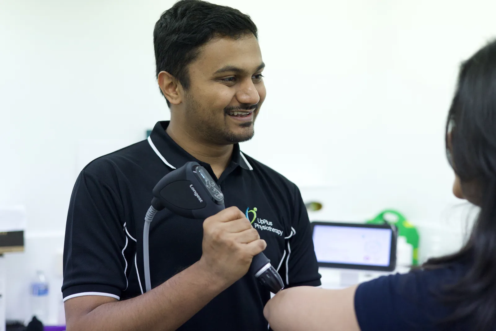 An UpPlus physiotherapist treating a patient's arm with the shockwave therapy handpiece